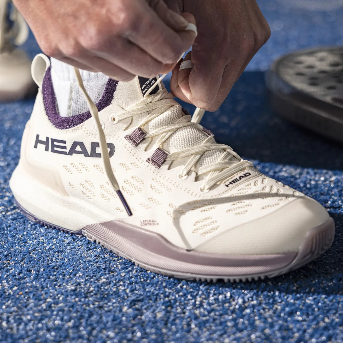 Player lacing the Head Motion Pro 1.5 women's padel shoes on a padel court